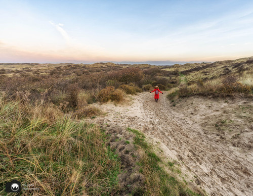 laura op de rug gezien met open armen in een duinpan
